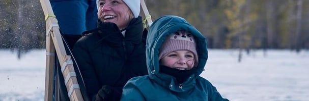 Close-up of mother and child sitting in dog sled and another adult steering the sled