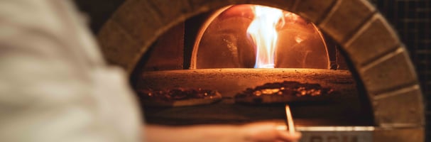 Pizza baker taking pizza out of pizza oven