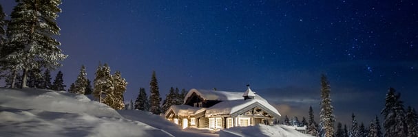 Evening photo of a cabin in a winter landscape, with lights in the windows