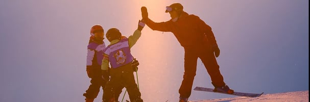 Ski instructor takes high five with two children on the slalom slope