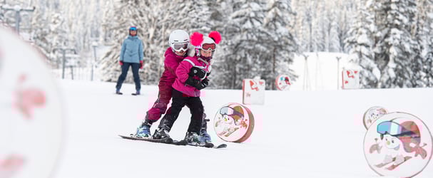 Two girls in pink clothes and pink tassels on their helmets race together in slalom