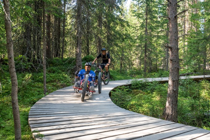 Two riding on adapted trails, one of them on an adaptive mountain bike with three wheels