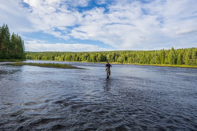 Man with fly fishing rod stands out in the river fishing